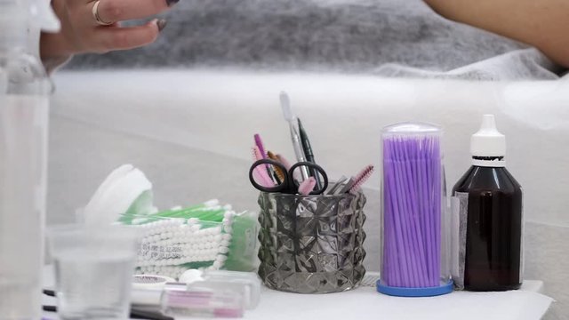 A master is taking a q-tip from table with different tools. The necessary things for the lamination of eye lashes are there.
