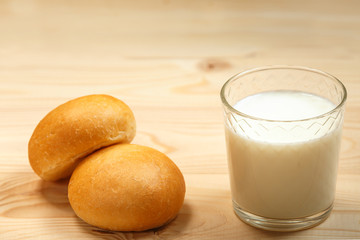 A glass of milk and two buns on a wooden background