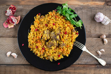 Dish of oriental cuisine - pilaf with lamb in a pan, on a wooden background.