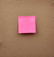 blank pink square paper glued on a brown cardboard surface