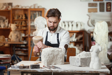 Stone carver works with wooden hammer and chisel at limestone. - obrazy, fototapety, plakaty