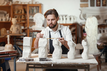 Male craftsman in working uniform makes a limestone copy of woman torso at the creative studio and...