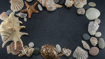 Frame of seashells, sea smooth stones and starfish on black granite with white spots background