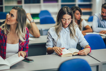 College students sitting at desk and studying together, a girl is reading a book.