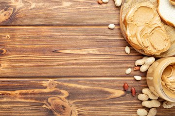 Toast sandwich with peanut butter. Spoon and jar of peanut butter and peanuts for cooking breakfast on a brown wooden background. Creamy peanut paste flat lay with place for text.