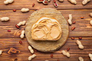 Toast sandwich with peanut butter. Creamy peanut paste on a piece of bread. Peanuts in the peel scattered on the brown wooden table with copy space for cooking breakfast. Vegan food concept