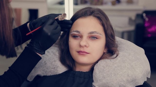 Professional master eyebrow woman paints eyebrows to client with brush in a beauty salon.