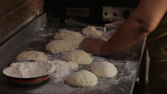 Hands of an elderly married woman knead the dough. She rolls the dough into pieces to make pita bread or pizza. Cooking food