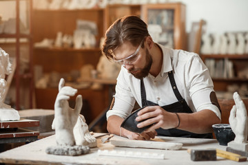 Young sculptor works in a plaster workshop. Craftsman pours gypsum into the silicone mold.