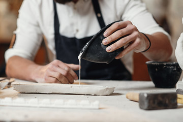 Young sculptor works in a plaster workshop. Craftsman pours gypsum into the silicone mold.