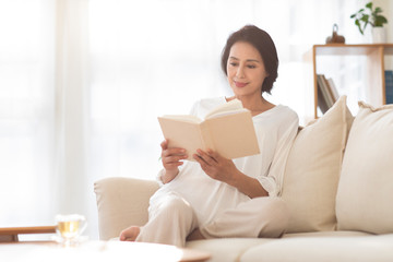 Mature woman reading book on sofa