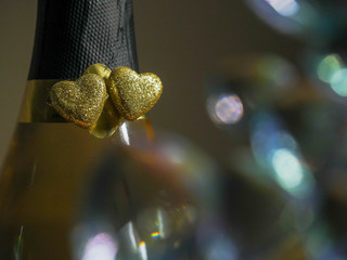 Tow golden hearts symbol of love on a neck of champagne bottle, abstract Saint Valentine background. Blurred glass in foreground.