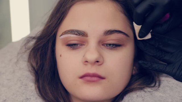 Professional woman eyebrow master cleans eyebrows to client in beauty salon.