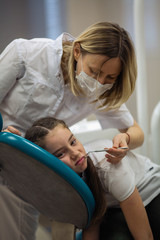 Dentist doing teeth checkup of little girl looking afraid and sad in a dental clinic.