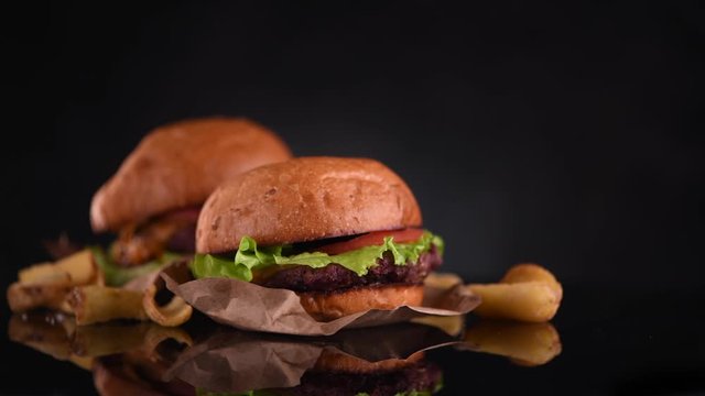 Hamburger and Double Cheeseburger with fries rotated on black background. Cheeseburgers on fresh buns with succulent beef patties and fresh salad ingredients served with French Fries. 4K UHD video.