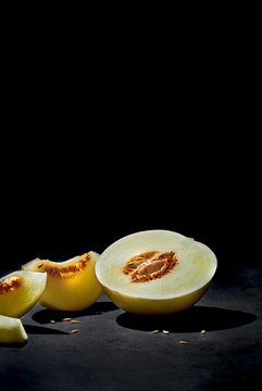 Bisected ripe fresh melon with seeds and tasty pieces under light in dark room