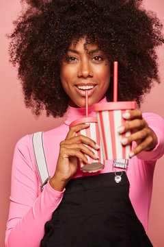 Happy black woman with disposable cup of drink standing against pink background
