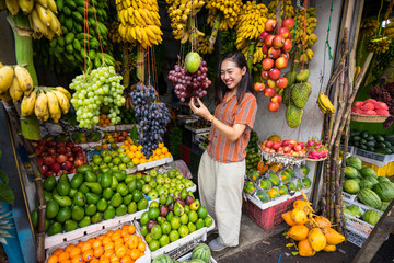 From above of Asian pleased woman on vacation in casual clothing making choice of fresh fruits at market at Sri Lanka