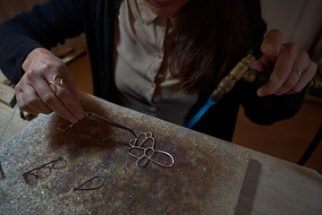 Cropped unrecognizable artisan woman jeweler working with torch welding jewels