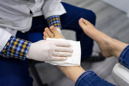 Crop male podiatry doctor in protective gloves cleaning foot of female patient with white napkin after performing ultrasound diagnostics