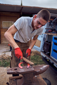 Blacksmith boy working on the anvil changing the horseshoe to a leg with tools