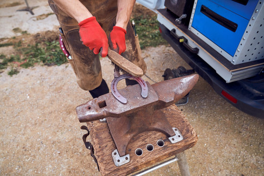 Cropped unrecognizable blacksmith boy working on the anvil changing the horseshoe to a leg with tools