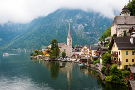 Clean pond with tranquil water and lovely houses of small town located near mountain ridge on cloudy day in Austria