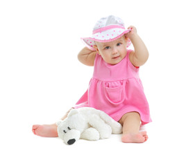 A little baby girl in pink dress and panama hat sits on white background in studio with little bear cub, isolated © Evgesha