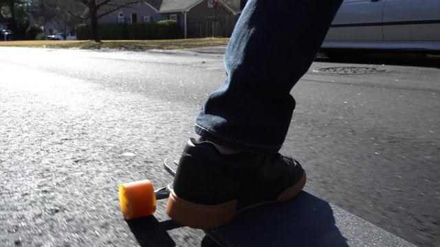 Close up of a skateboard and feet as a person rides his long board down a street - slow motion