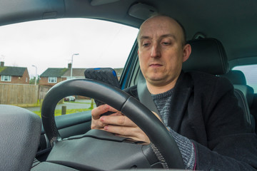 A middle aged man sat in the driver's seat of a car using a mobile phone.