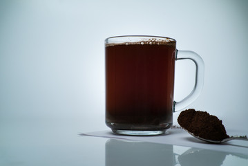 transparent cup with natural coffee and a spoon of ground coffee on a light background with free space for text