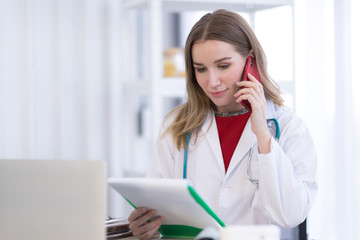 A female doctor wearing a white coat talking on the phone with a patient