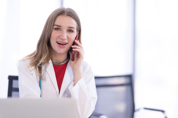 A female doctor wearing a white coat talking on the phone with a patient