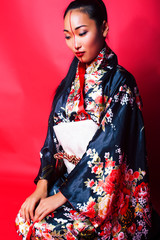 young pretty geisha on red background posing in kimono, oriental concept