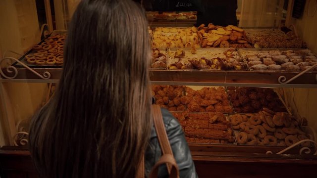Long-hair brunette woman shopping desserts at candy shop looking at the showcase makes a choice of traditional Italian sweets