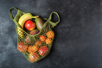Fresh fruit in a green string bag on a black background. Bananas, apples, oranges, and mangoes.