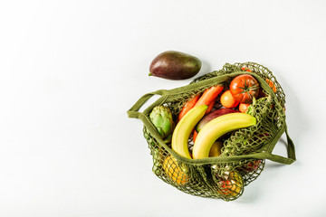 Fresh vegetables and fruits in a green string bag on a white background. No plastic, only natural materials and natural products.