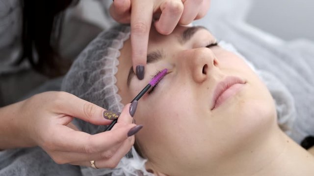 A lash maker is brushing the eye lashes. The professional have laminated and dyed the lashes. The esthetician is using a one-time brush.