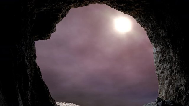 Looking out a cave entrance as the sun shines into the tomb against a dramatic moody sky.