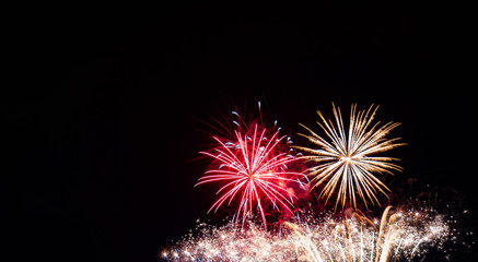 Red starburst firework, gold starburst firework over multiple gold sparkling streamers with a black background