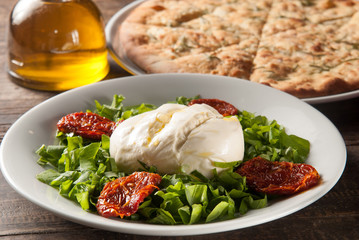front view of dish with burrata, arugula and sun-dried tomatoes, olive oil and focaccia