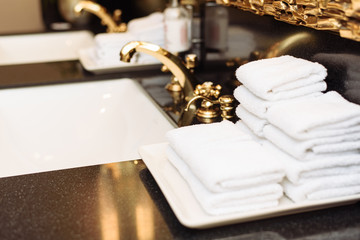 A stack of fresh white towels in the hotel's luxurious bathroom. A gold faucet, mirror and marble...
