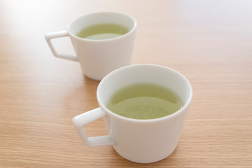 Obraz na płótnie Canvas シンプルなマグカップに入れた緑茶　２つ　2人　２人　ふたり　二人　余白　ホワイトスペース　文字スペース　コピースペース　空白　背景　背景素材　グラフィック背景　グラフィック素材　木目　木　テーブル　机　上