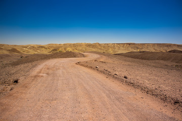 Israeli Negev desert landscape dry ground scenic view curved trail go to horizon background with sand stone rocks mountain ridge, copy space