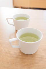 シンプルなマグカップに入れた緑茶　２つ　2人　２人　ふたり　二人　余白　ホワイトスペース　文字スペース　コピースペース　空白　背景　背景素材　グラフィック背景　グラフィック素材　木目　木　テーブル　机　上