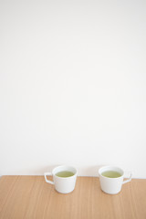 Obraz na płótnie Canvas テーブルの上にある２つのマグカップ　緑茶　２つ　２人　二人　ふたり　お茶　茶　イメージ　休憩　余白　ホワイトスペース　文字スペース　コピースペース　部屋　白　壁　机　テーブル　カフェ