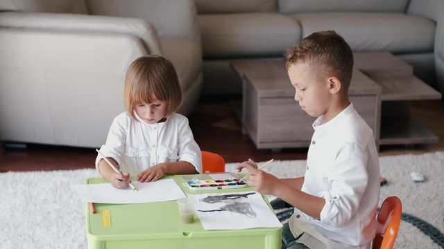 The kids are drawing. They are sitting. Children use the paint.