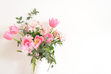 Obraz na płótnie Canvas シンプルな花瓶とピンク系の花　ピンク系の花とグリーン　花瓶　白い花瓶　　部屋　白壁　白背景　室内　屋内　自然光　余白　ホワイトスペース　コピースペース　文字スペース　縦　背景素材　背景　グラフィック素材　　白　緑　ピンク　春　季節　スイートピー