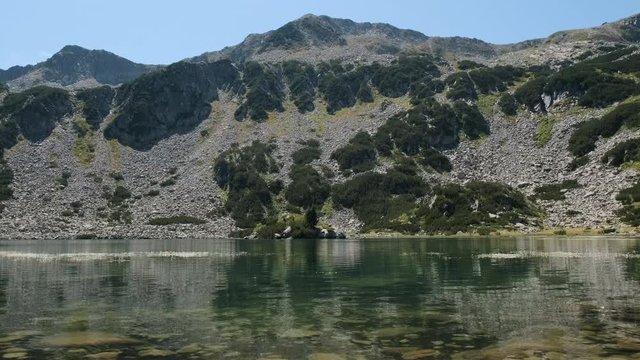 Panorama of beautiful green mountains, blue sky, flying birds and the calm surface of a mountain lake in summer on a sunny day. Idyll in nature. Relax