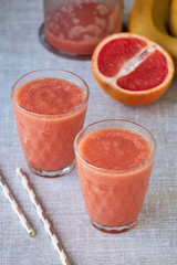 Two glasses of grapefruit smoothie on a gray background 
